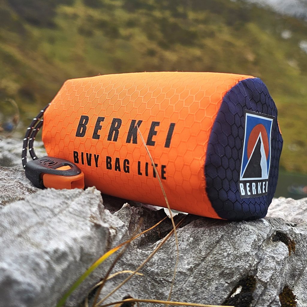 BERKEI Bivy Bag Lite in orange mit schwarzem Logo auf Steinen in der Natur
