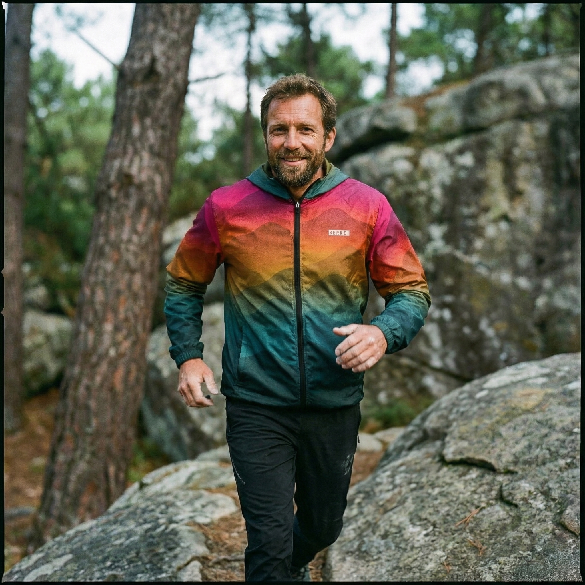 Mann im BERKEI Windbreaker Unisex Forest Sunrise beim Laufen auf Felsen