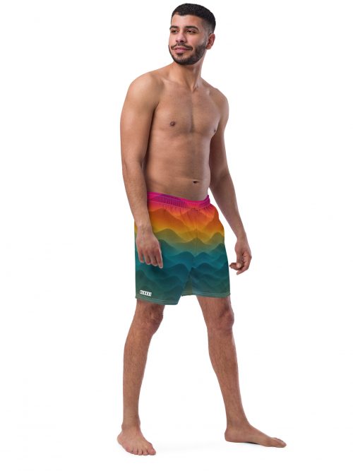 Mann trägt BERKEI Badehose Forest Sunrise mit buntem Wellendesign am Strand.
