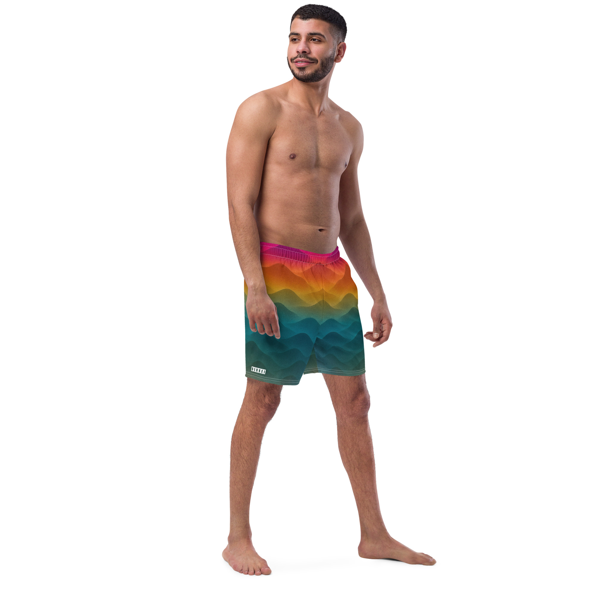 Mann trägt BERKEI Badehose Forest Sunrise mit buntem Wellendesign am Strand.