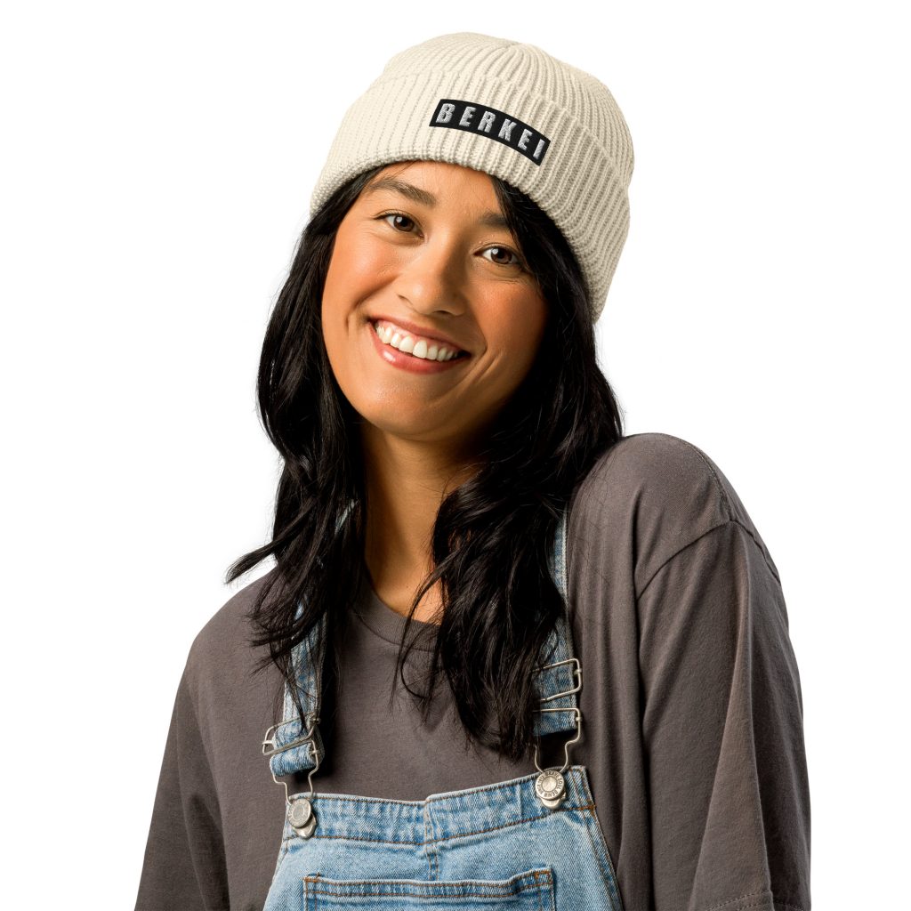 Junge Frau trägt beigen BERKEI Beanie, lächelnd in lässiger Kleidung.