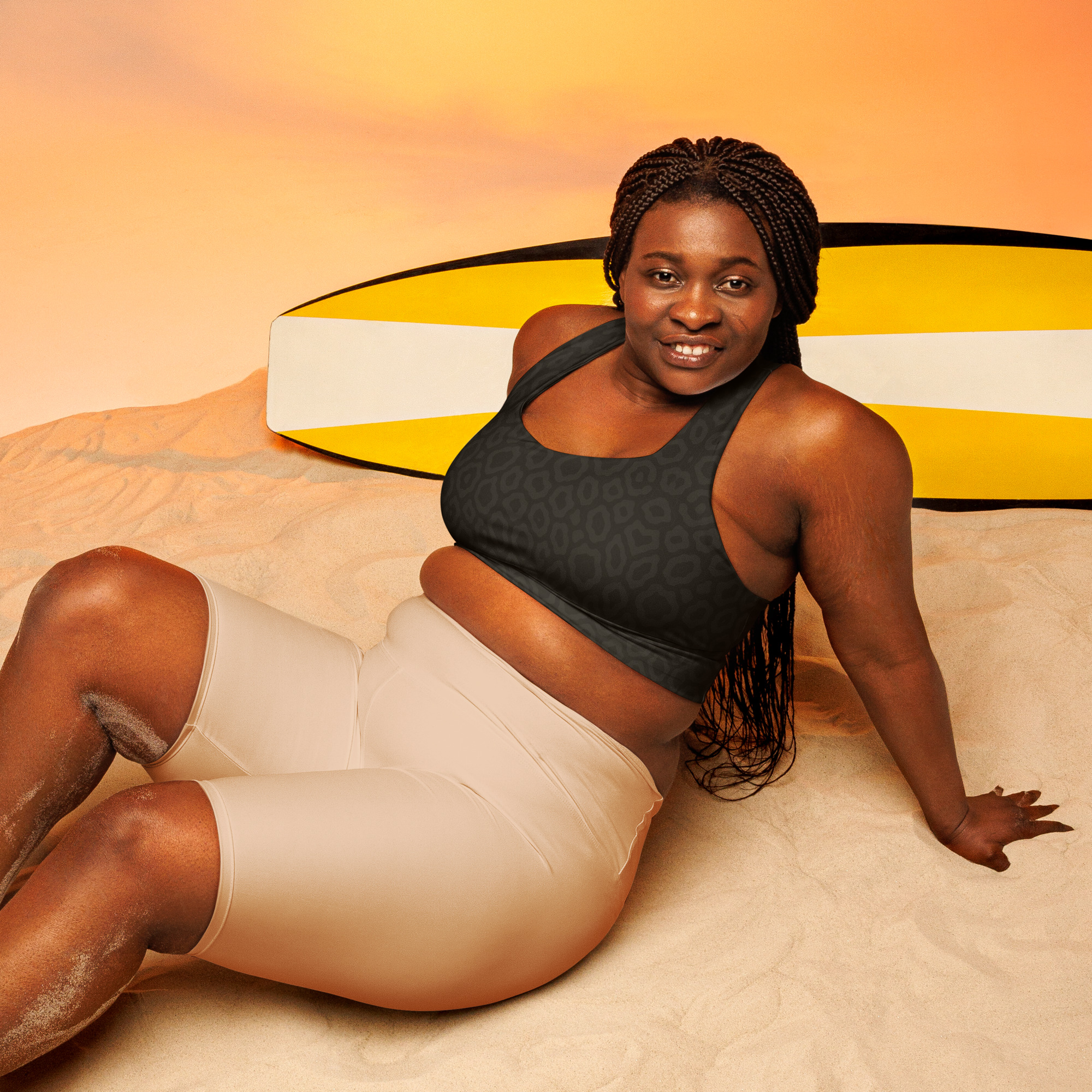 Sportliche Frau trägt BERKEI Sport-BH Midnight Leo High Intensity am Strand mit Surfbrett.