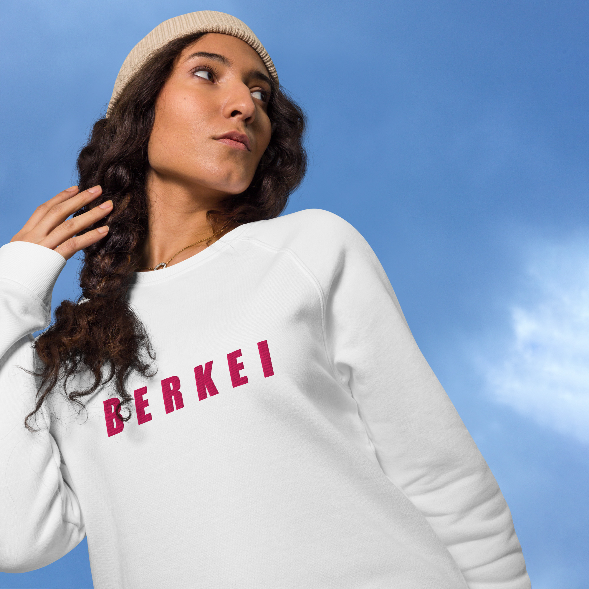 Frau trägt weißen BERKEI Unisex Bio Pullover vor wolkigem Himmel