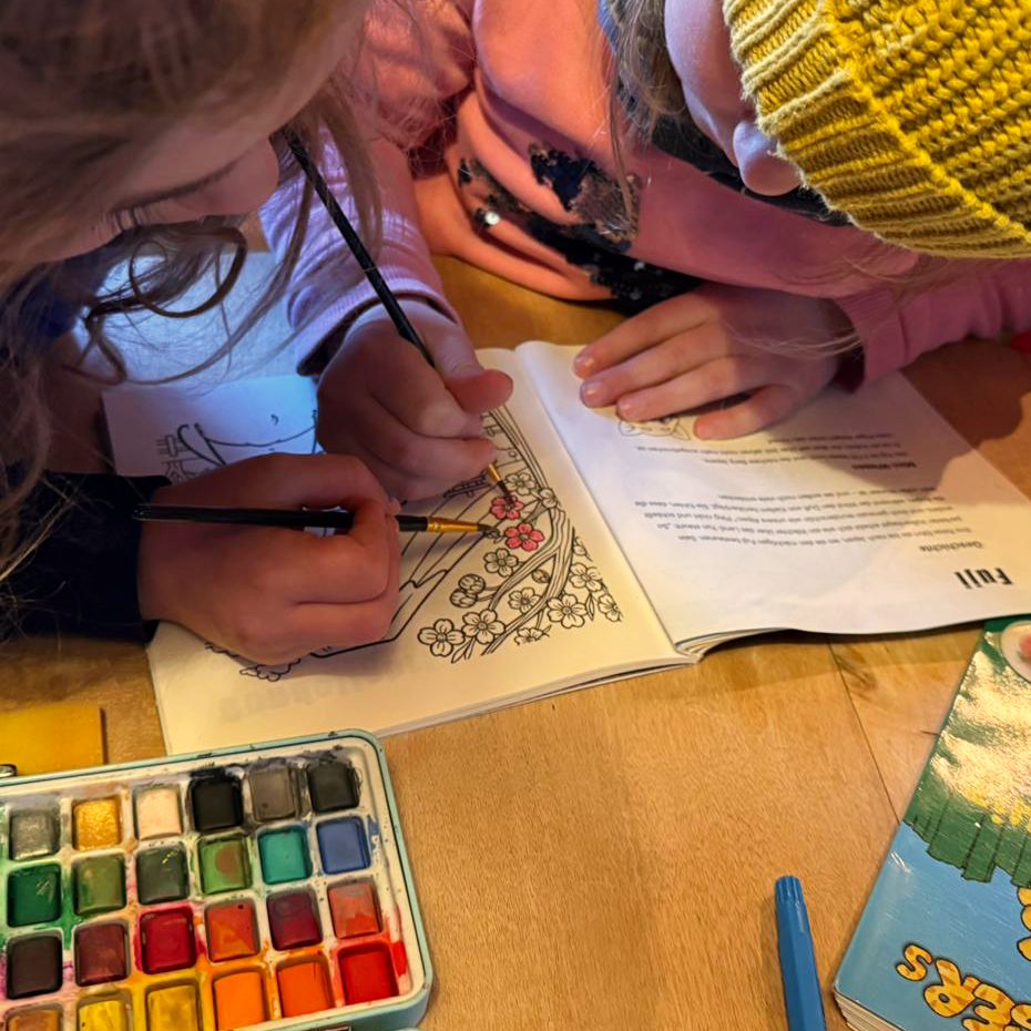 Zwei Kinder malen im BERKEI-Ping & Yun Alpenüberquerung Malbuch mit Aquarellfarben.