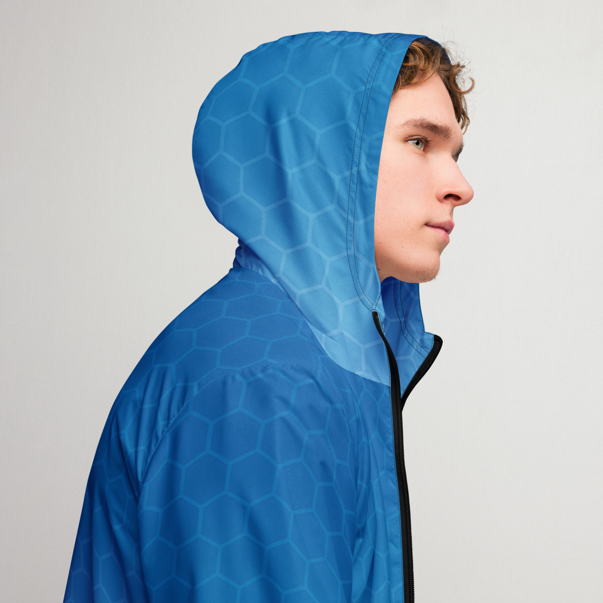 Junger Mann trägt BERKEI Windbreaker Blue Gear mit trendigem Design in einer neutralen Umgebung.