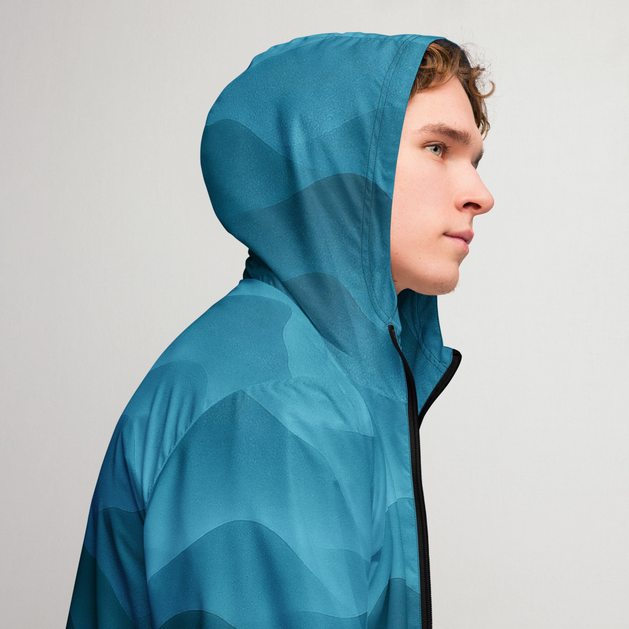 Junger Mann trägt BERKEI Windbreaker in Fountain Blue Farbe mit Kapuze.