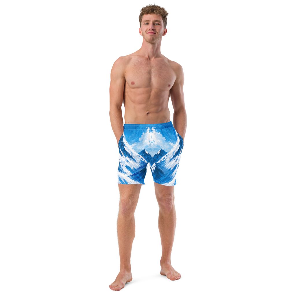 Mann trägt BERKEI Badehose Alpine Rush mit blauem Bergdesign beim Stehen auf der Küste